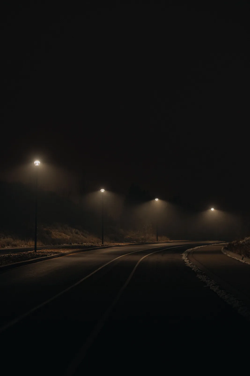 A dark, empty road lit by streetlights at night